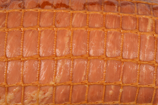 A close up shot captures the detailed surface of a smoked ham with a glossy texture wrapped in a yellow elastic netting
