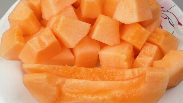 Close-up of juicy orange-fleshed cantaloupe cubes neatly arranged on a rotating white plate.