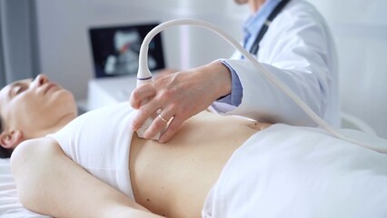 Doctor man, wearing white medical gloves, is using ultrasound equipment on the breast of a female patient lying down for a medical cardiology examination. Medicine concept © volha_r