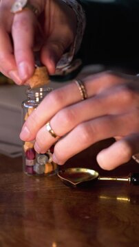vertical video. A girl seals a letter with a wax seal. A woman holds an old spoon and heats wax in a golden spoon over a candle, preparing to seal the letter. Wax seal. Sending mail.