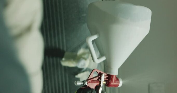 Spray gun applying paint from hopper onto wall surface close up