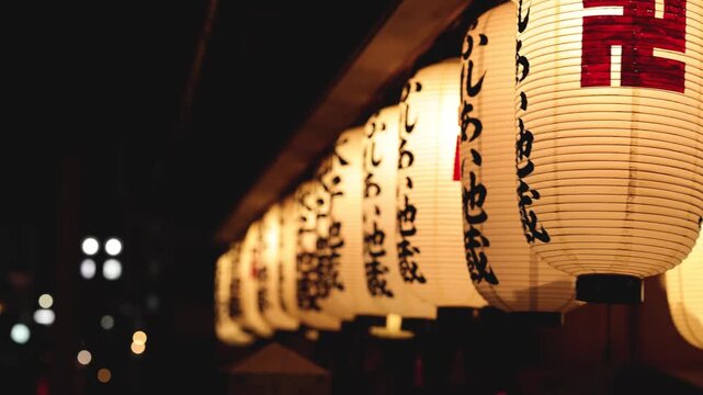 Row of traditional japanese paper lanterns hanging at buddhist temple night festival with motion.