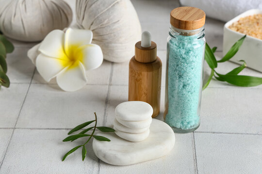 Set of spa accessories with stones, plant branches and plumeria flower on white tile table