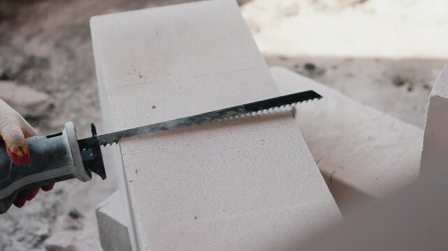 Cutting aerated concrete block with hand saw during construction close up