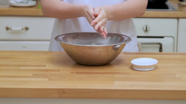 Person is making something in a bowl on a wooden table. The bowl is silver and filled with a white substance