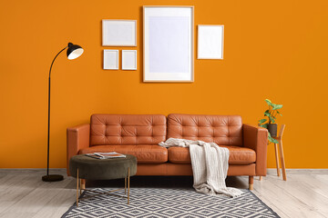 Interior of stylish living room with brown sofa, ottoman and standard lamp near orange wall