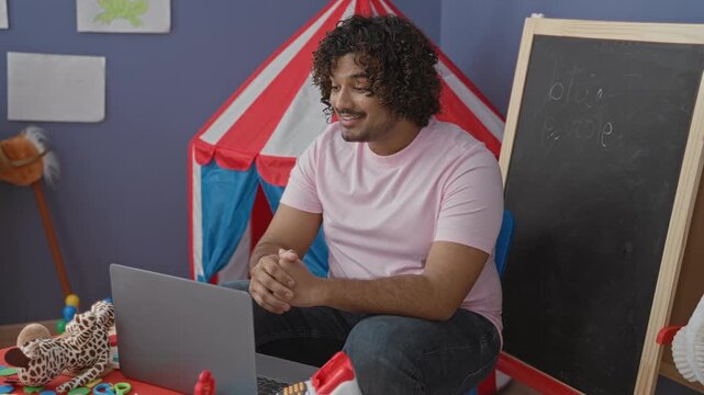 Man indian young holds giraffe puppet and gestures to laptop in kindergarten play tent inside a school building; nurturing joy.