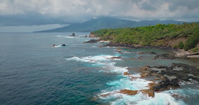 Aerial footage of ugged coastline of Port Resolution on Tanna Island, Vanuatu, breaking waves against volcanic rocks, lush tropical jungle vegetation and a secluded white sand beach. Natural landscape