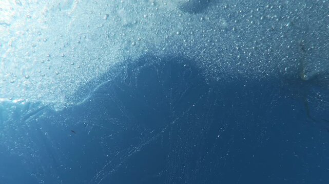 Sunrays explodes through of drifting ice floe, illuminating thousands of trapped air motes like tiny diamonds. Close-up of shimmering, glass-like texture of ice as it glimmers against vibrant blue sky