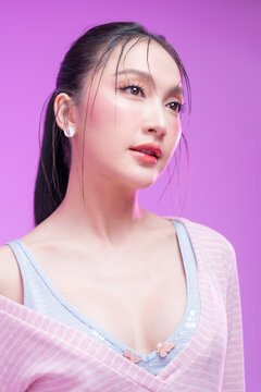 Beautiful young Asian woman with glowing skin and trendy wet hair look posing against a pastel pink background; elegant fashion portrait showcasing skincare, facial treatment, and Gen Z aesthetic.