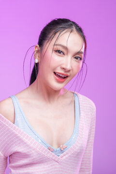 Beautiful young Asian woman with glowing skin and trendy wet hair look posing against a pastel pink background; elegant fashion portrait showcasing skincare, facial treatment, and Gen Z aesthetic.