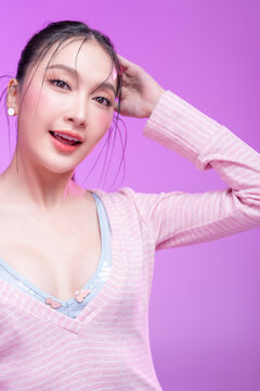Beautiful young Asian woman with glowing skin and trendy wet hair look posing against a pastel pink background; elegant fashion portrait showcasing skincare, facial treatment, and Gen Z aesthetic.