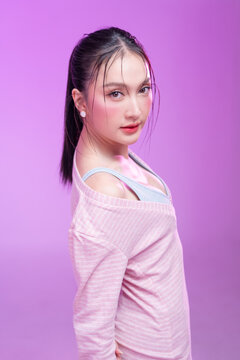 Beautiful young Asian woman with glowing skin and trendy wet hair look posing against a pastel pink background; elegant fashion portrait showcasing skincare, facial treatment, and Gen Z aesthetic.