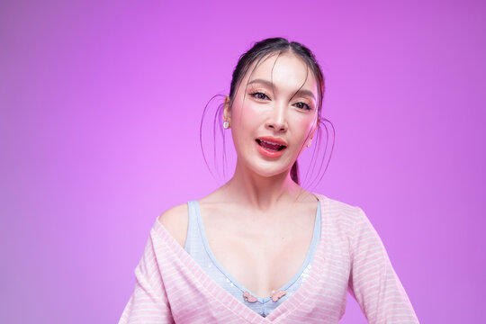 Beautiful young Asian woman with glowing skin and trendy wet hair look posing against a pastel pink background; elegant fashion portrait showcasing skincare, facial treatment, and Gen Z aesthetic.