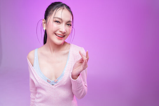 Beautiful young Asian woman with glowing skin and trendy wet hair look posing against a pastel pink background; elegant fashion portrait showcasing skincare, facial treatment, and Gen Z aesthetic.