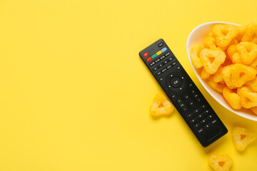 Fototapeta premium Modern TV remote control with bowl of puffed corn triangles on yellow background