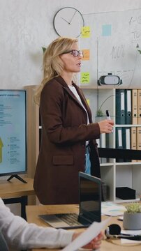 Ambitious business woman draws a graph on glassboard with stickers during a presentation in conference room. Business female team brainstorming. Slow motion