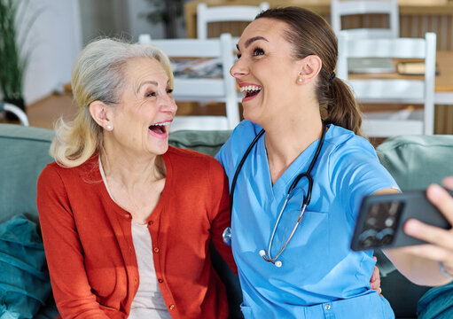Doctor or nurse caregiver helping senior woman with a mobile phone taking selfie at home or nursing home