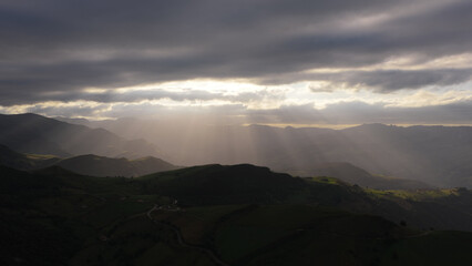 Obraz premium Cantabria mountain ranges receiving bright sunbeams through an overcast sky, creating a moody and atmospheric landscape