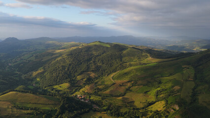 Cantabrian green hills and valleys bathed in warm morning light under a dramatic cloudy sky, serene rural landscape from above © DMegias