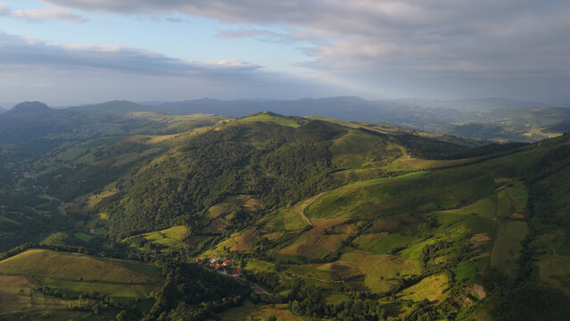 Cantabrian green hills and valleys bathed in warm morning light under a dramatic cloudy sky, serene rural landscape from above