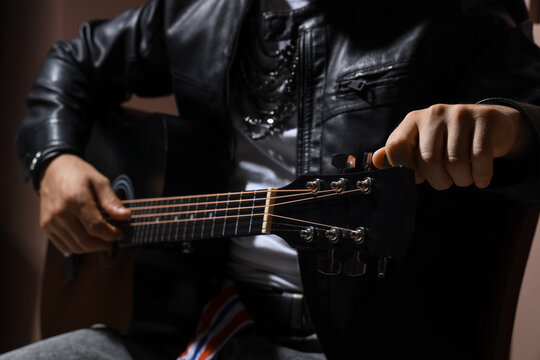 Young man in leather jacket playing guitar on brown background