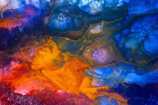 Colorful abstract art created with paint on a surface, showing deep blue and bright orange blending in unique shapes, captured in a studio setting