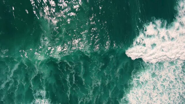 Aerial shot of the ocean with waves doing swirls and patters, rocks, sand and beach