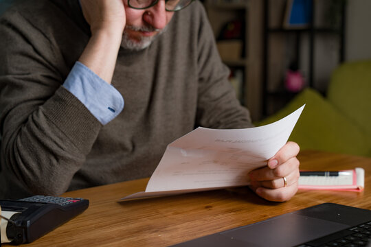 Mature man reviewing bills at home with concerned expression and financial stress