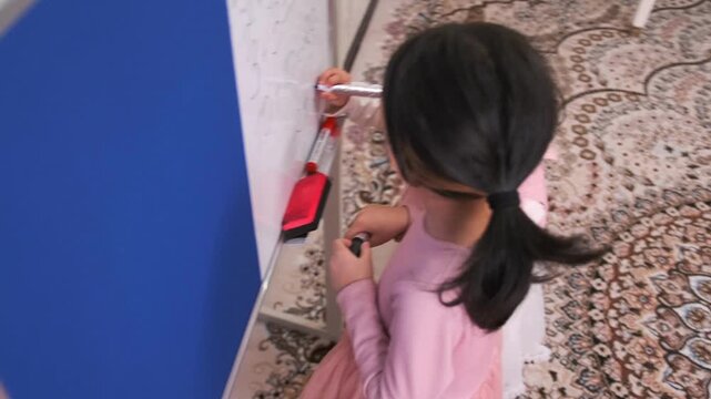 Little girl wipes whiteboard with eraser while playing school at home, acting like teacher and learning through role play, education concept, childhood creativity and imagination
