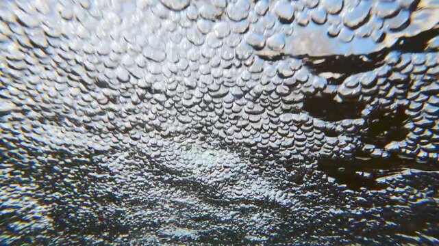 Slow motion of rapidly rushing flow of air bubbles across surface of water. Close-up of aerated bubbles rapidly flowing on surface. Water foaming in rapid stream quickly rushing towards camera