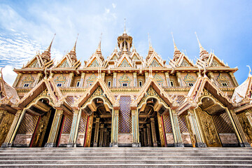 Obraz premium Intricate golden Thai Buddhist temple architecture with multiple spires against blue sky.