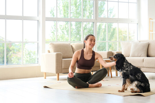 Sporty young woman with cute dog sitting on yoga mat at home