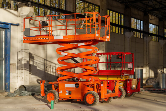 Two orange scissor lifts of different sizes parked inside an old industrial warehouse hall