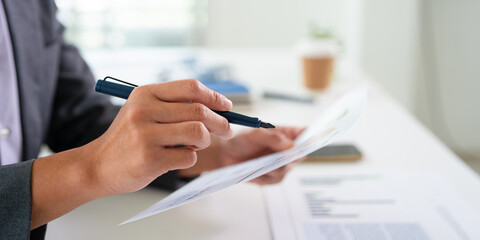 Fototapeta premium Close up hnads holding pen reviewing document papers at desk.