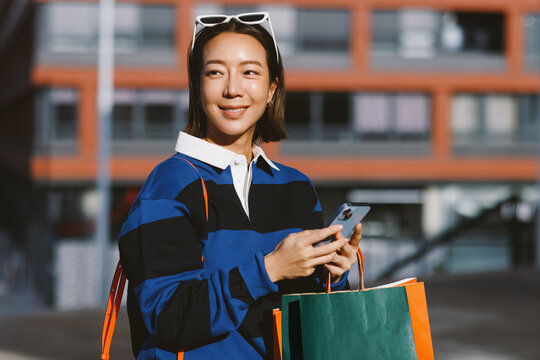 Asian woman smiling holding smartphone and shopping bags