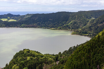 Fototapeta premium View of Furnas Lake from Pico do Ferro Viewpoint. Lush greenery surrounds the lake with the Atlantic Ocean visible in the distance. Sao Miguel Island, Azores, Portugal.