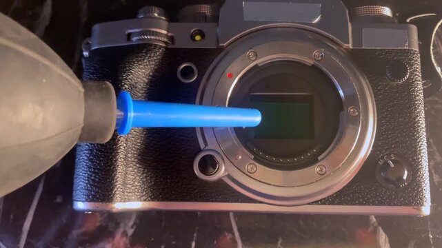 air blower cleaning camera sensor close-up, removing dust from matrix inside body, careful maintenance process for photography equipment and image quality protection