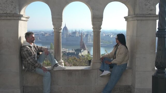 Two friends enjoy stunning panoramic views of Budapest from Fisherman Bastion, sharing laughter and moments of joy against the magnificent cityscape. A perfect day for sightseeing.
