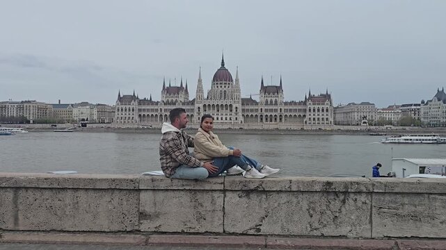 Enjoy serene views of Budapest as a traveler sits by the Danube River, admiring the majestic Parliament building. This picturesque location captures the heart of Hungarys rich culture.