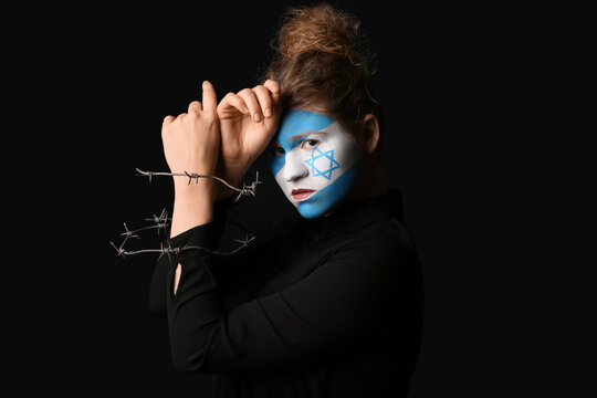 Young woman with painted flag of Israel on her face and barbed wire against black background. International Holocaust Remembrance Day