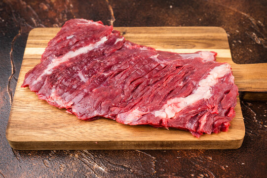 Top view of raw beef bavette flap steak with peppercorn spices and carving fork. Butcher style machete hanger skirt type cut on textured brown surface.