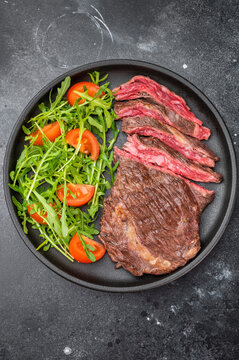 Juicy grilled diaphragm steak skirt served with arugula and tomatoes on dark textured background
