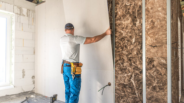 Making a plasterboard partition. A worker is laying drywall board on a metal support structure of partition.