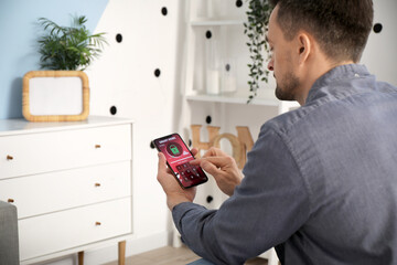 Naklejka premium Young man using mobile phone with smart home security system control panel in bedroom, back view