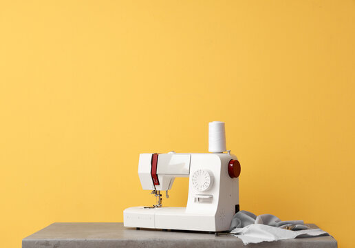 Modern sewing machine with fabric on yellow background