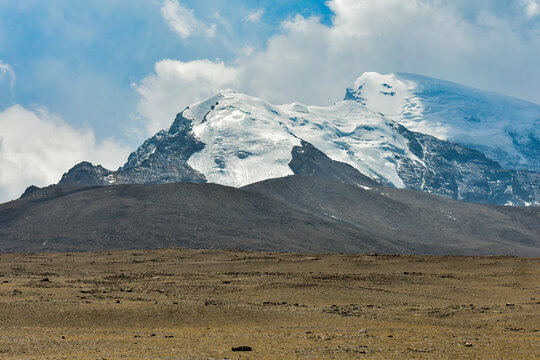Snowy Himalayan mountain in North Sikkim dominates a rugged plateau beneath a serene sky with clouds.