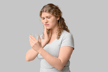 Fototapeta premium Beautiful young woman with glass of water suffering from toothache on grey background