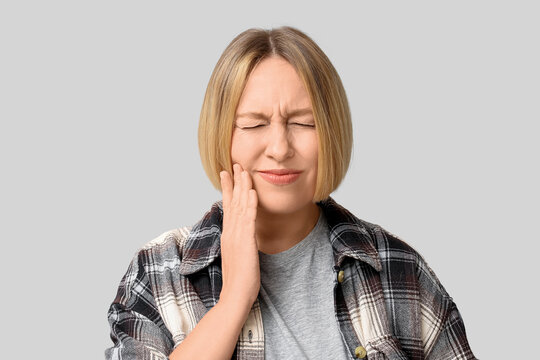 Beautiful mature woman suffering from toothache on grey background