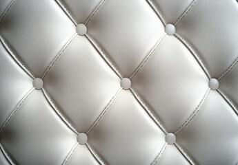 Fototapeta premium Close-up of cream tufted leather upholstery with round buttons and stitched diamond pattern, evoking luxurious comfort and elegant calm